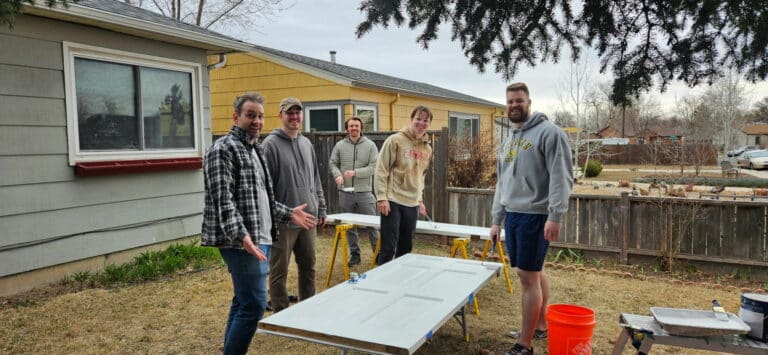 group of five white young adult males standing around two doors they are painting white