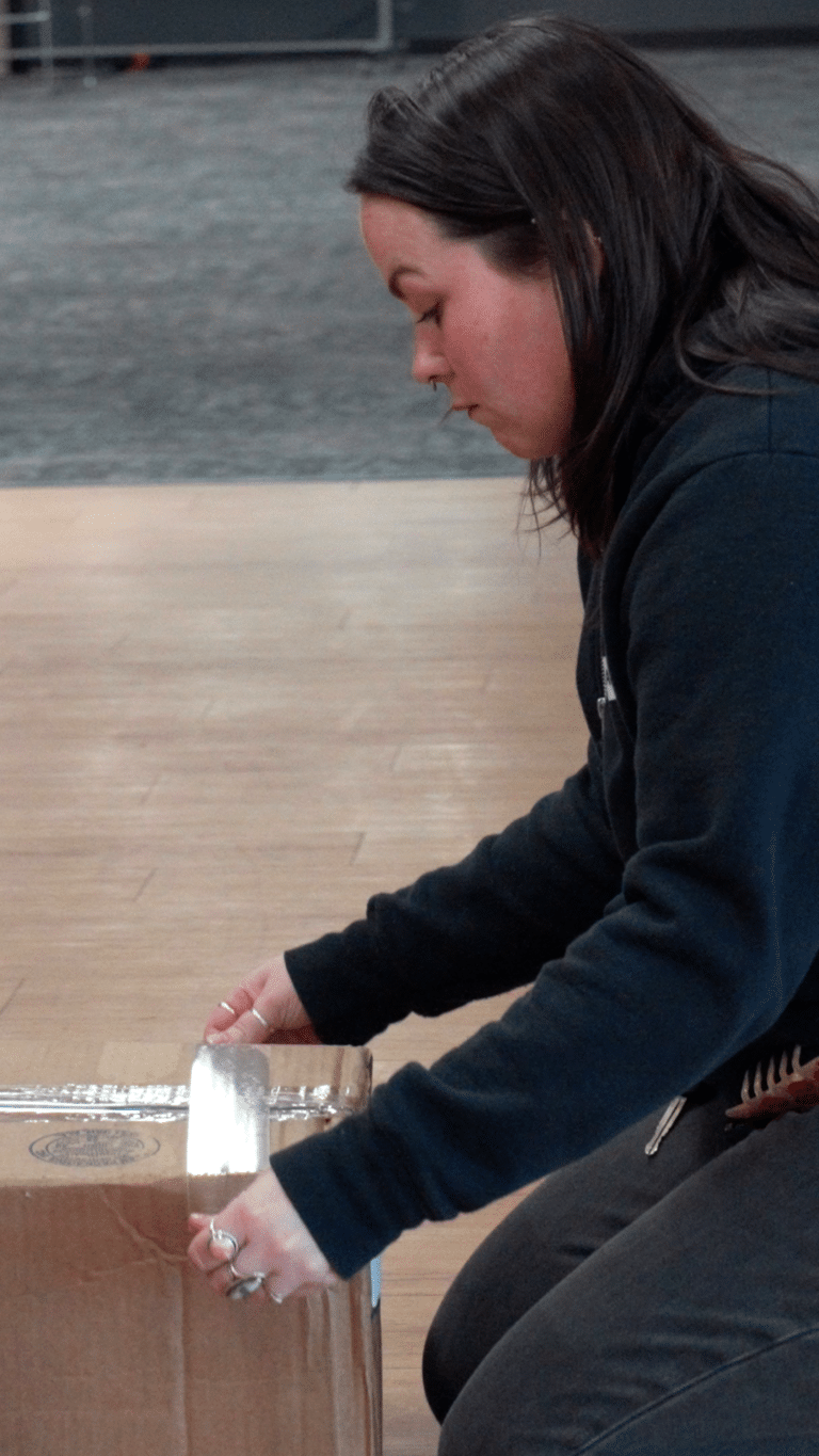 white young adult female wearing black taping a box closed