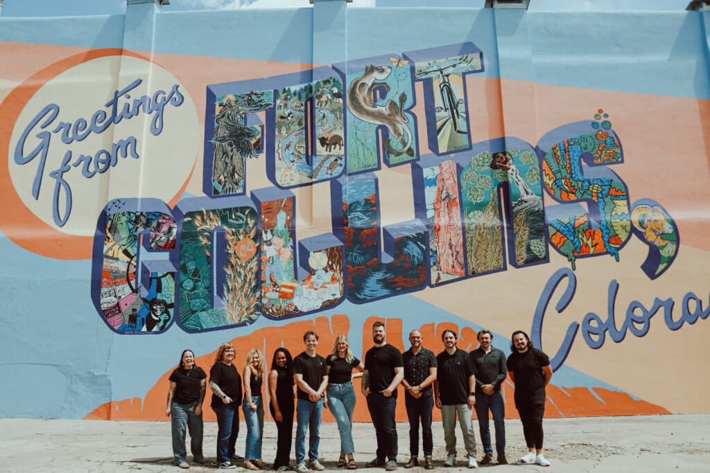 A group of people standing in front of the Welcome to Fort Collins, Colorado sign in Old Town, Fort Collins